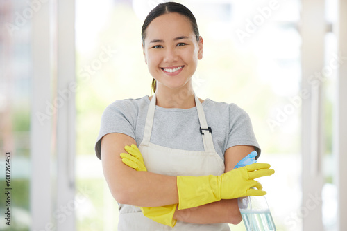 Portrait, cleaning and arms crossed with a woman housekeeper using disinfectant to remove bacteria in a home. Safety, smile and hygiene with a confident young female cleaner working in a living room photo