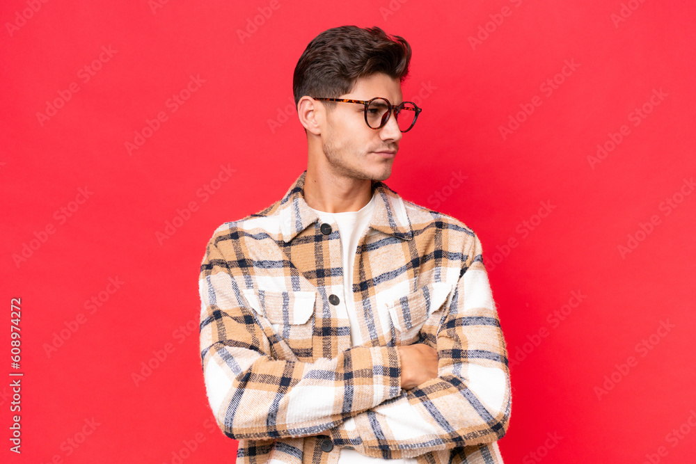 Fototapeta premium Young caucasian handsome man isolated on red background keeping the arms crossed