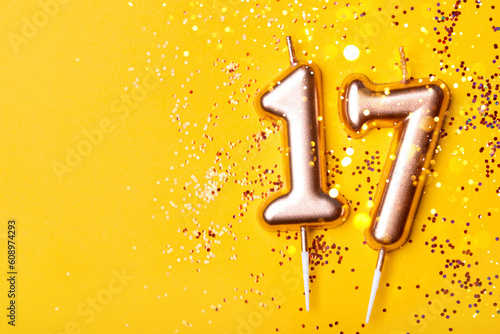 Gold candles in the form of number seventeen on yellow background with confetti. 17 years celebration.