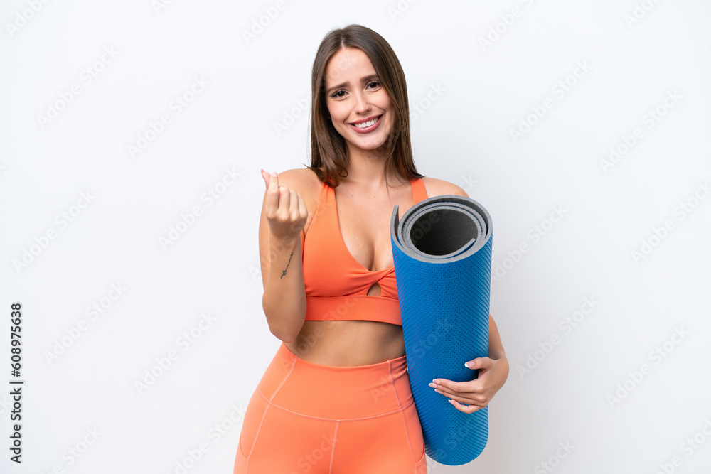 Young beautiful sport woman going to yoga classes while holding a mat isolated on white background making money gesture Young beautiful sport woman going to yoga classes while holding a mat isolated on white background making money gesture