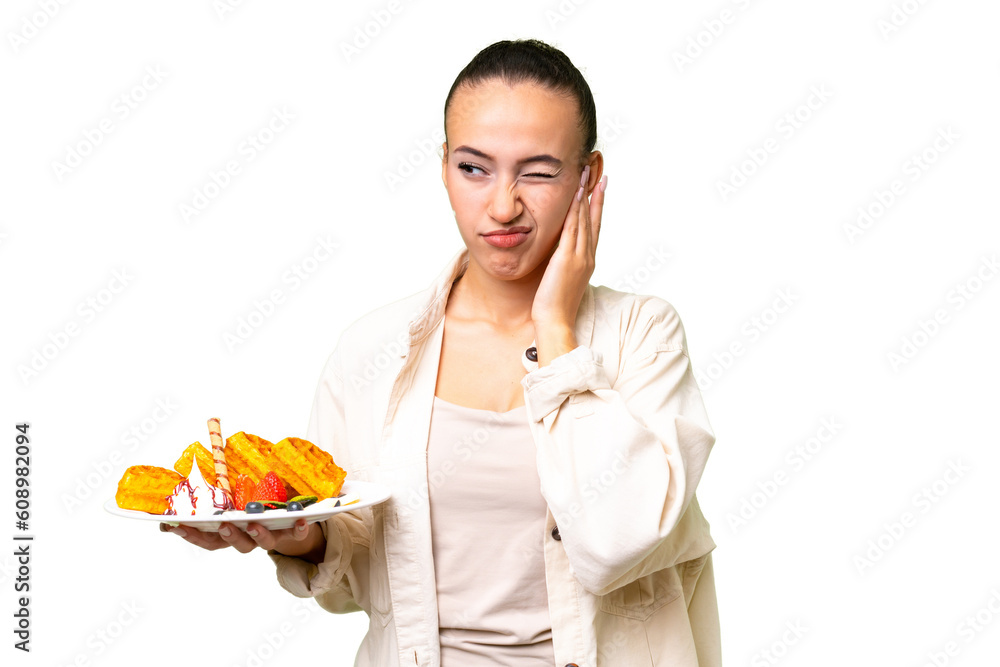 Young Arab woman holding waffles over isolated background frustrated and covering ears Young Arab woman holding waffles over isolated background frustrated and covering ears