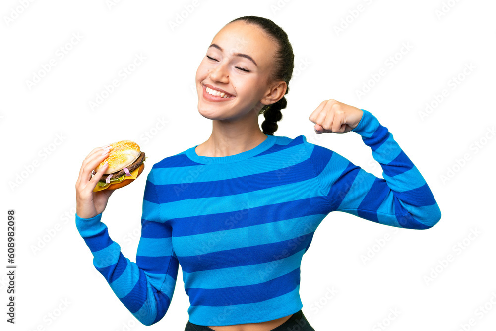 Young Arab woman holding a burger over isolated background doing strong gesture Young Arab woman holding a burger over isolated background doing strong gesture