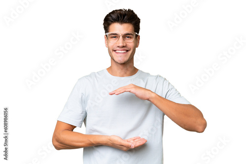 Young caucasian handsome man over isolated background holding copyspace imaginary on the palm to insert an ad