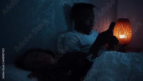 Man smiles and looks over at partner while they lay in bed at night using a smart phone