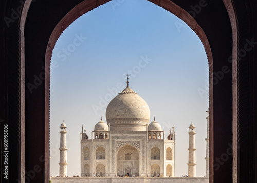 A majestic Tajmahal, one of the world's seven wonders is viewed through its dark brown archways. A clear blue sky adds magnificence to the white marble of the beautiful architectural structure.