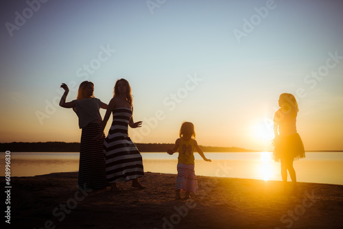 Silhouette of groupe dancing people at sunset. Childhood and motherhood happiness concept. Women and children. Summertime season. Joyful emotions. Summer vacation. Holidays. Birthday mood. Seascape