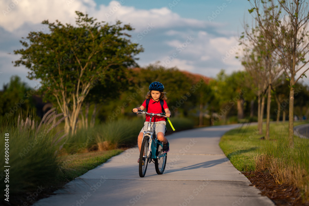 Fototapeta premium Sporty kid riding bike on a park. Child in safety helmet riding bicycle. Kid learns to ride a bike. Kids on bicycle. Happy child in helmet cycling outdoor. Sports leisure with kids.
