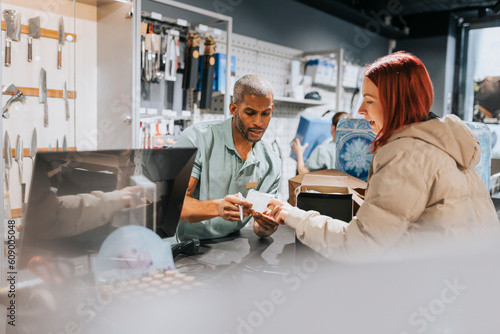 Male retail clerk showing bill to female customer at checkout in electronics store