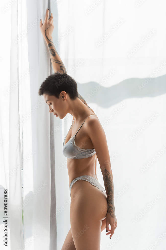 side view of irresistible woman with short brunette hair, tattooed arms and  sexy body standing with