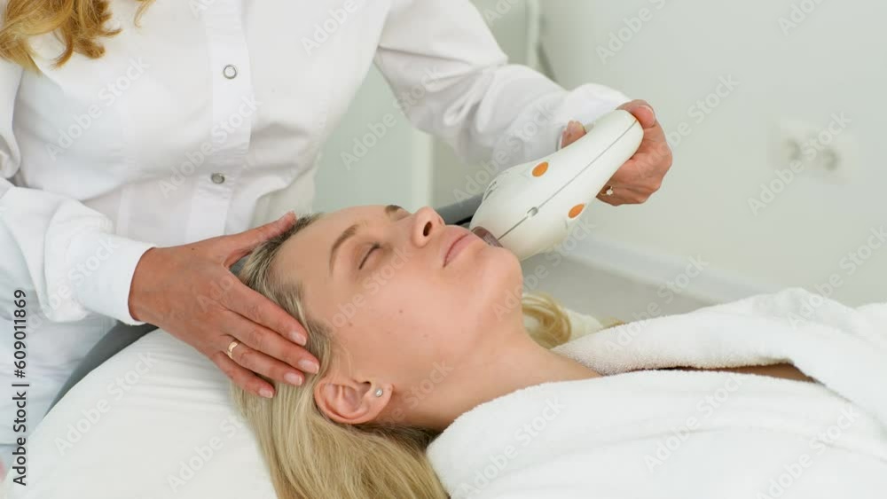 Close-up tracking shot of unrecognizable cosmetician performing photo rejuvenation cosmetology procedure for woman in modern beauty clinic, slow motion. Concept of anti-age rejuvenation skincare. Close-up tracking shot of unrecognizable cosmetician performing photo rejuvenation cosmetology procedure for woman in modern beauty clinic, slow motion. Concept of anti-age rejuvenation skincare.