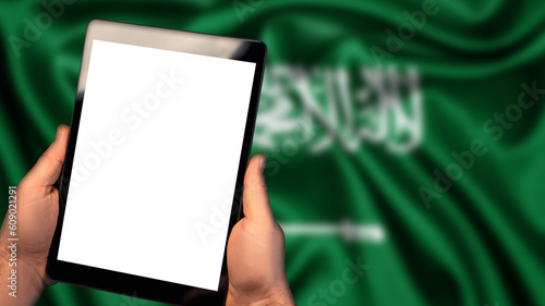 Man hold tablet phone pc gadget with white blank screen, copy space for text, image or message. Flag of Saudi Arabia country on background. Technology, information, business
