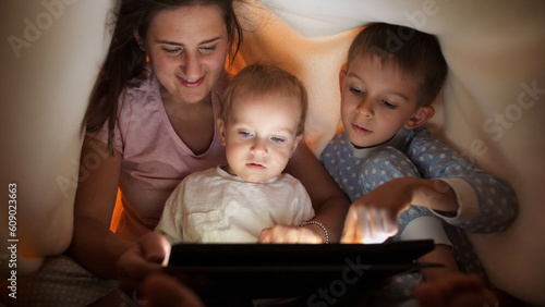 Happy cheerful family hiding under blanket and using tablet computer. Family having time together  parenting  happy childhood and entertainment.