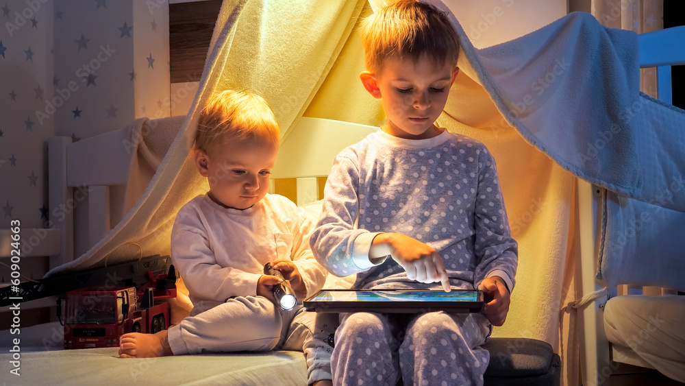 Two cute boys in pajamas playing games on tablet computer in bed at night.  Children with gadgets, education, kids development Stock Photo