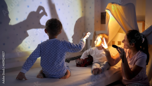 Young mother playing with flashlight and her two sons showing them shadows on wall