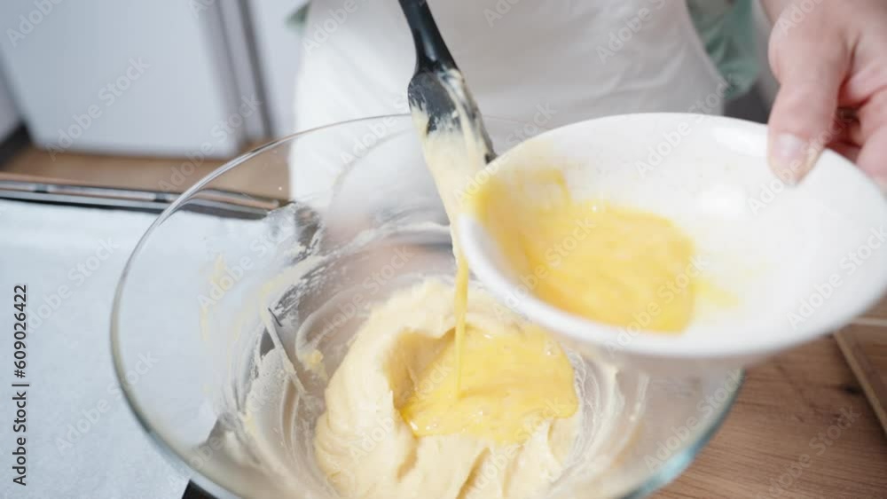 The woman in the white apron pours the beaten egg into the plate with the dough, in slow motion. The woman in the white apron pours the beaten egg into the plate with the dough, in slow motion.