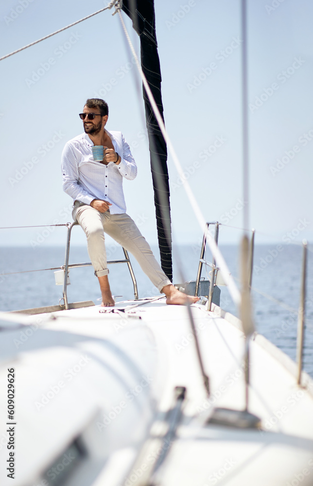 A young handsome male model at a photo shooting on a yacht on the seaside is enjoying a coffee and the sun. Summer, sea, vacation A young handsome male model at a photo shooting on a yacht on the seaside is enjoying a coffee and the sun. Summer, sea, vacation