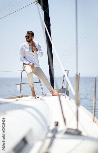 A young handsome male model at a photo shooting on a yacht on the seaside is enjoying a coffee and the sun. Summer, sea, vacation