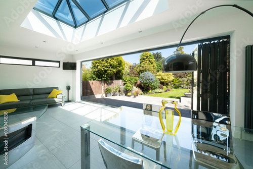 View from interior of designer, lifestyle, open-plan room through open bifold doors to beautiful patio and garden on summer day.