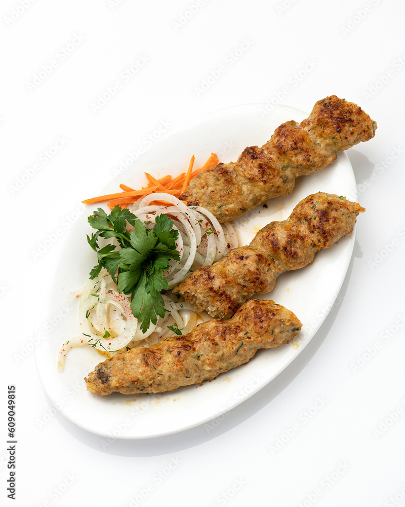 Three chicken kebabs with vegetables on white oval plate. Fried kebab with onions and carrots. Asian, Turkish cuisine. Fast food. White background. Top view. Copy space.
