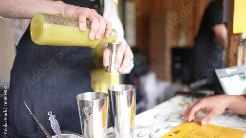 Cocktail bartender pouring yellow pineapple juice into a shot glass to shake and mix