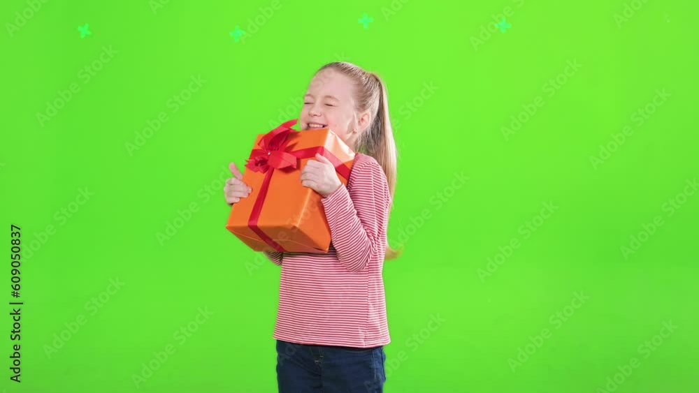 Curious little girl shaking big holiday gift box, guessing, what inside is, in motion. Front view of joyful female kid with ponytail hugging wrapped present, isolated on green. Celebration concept. Curious little girl shaking big holiday gift box, guessing, what inside is, in motion. Front view of joyful female kid with ponytail hugging wrapped present, isolated on green. Celebration concept.