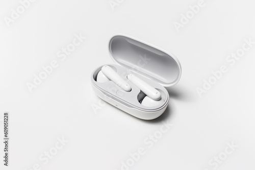 Close-up of modern wireless earbuds lying in opened charging case on white studio background.