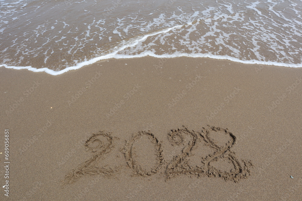 New Year 2028 written in the sand on a beach with sea wave background. New Year 2028 written in the sand on a beach with sea wave background.
