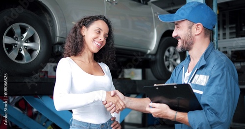 Happy automotive mechanic man in uniform shaking hands with women client at auto repair shop. Car service, repair, maintenance, gestures and man-mechanic concept