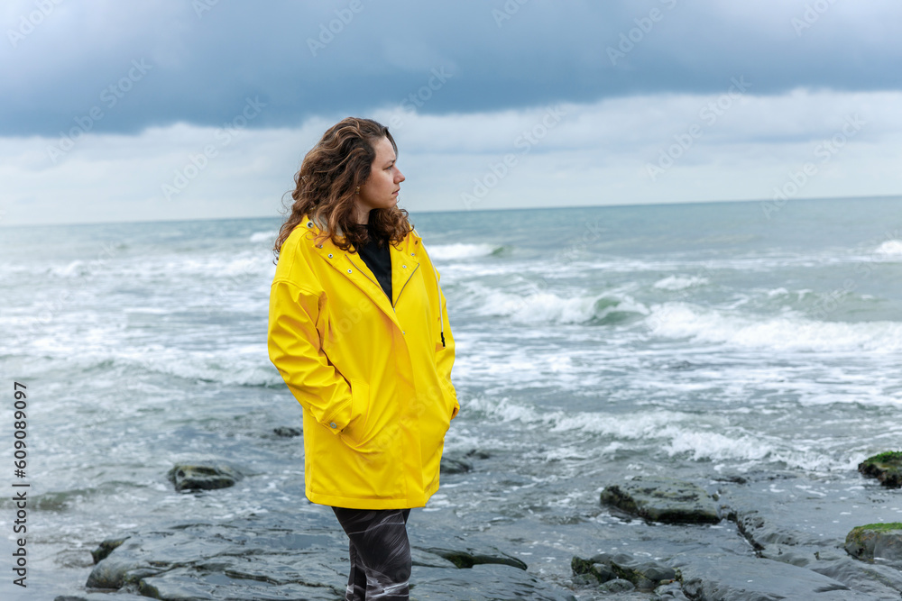 Woman wearing yellow raincoat walking on the beach on a rainy day Woman wearing yellow raincoat walking on the beach on a rainy day