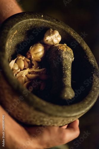 arms hold a large black traditional molcajete filled with garlic in low light photo