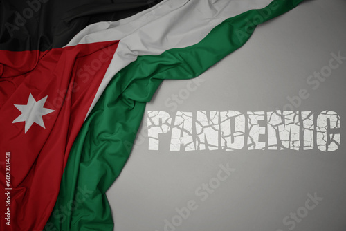 waving colorful national flag of jordan on a gray background with broken text pandemic. concept.