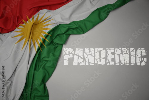 waving colorful national flag of kurdistan on a gray background with broken text pandemic. concept.