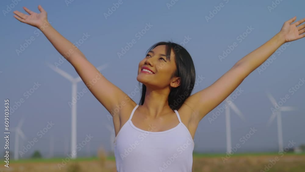 Young asian beautiful woman with enjoying expression at wind turbine farm. Electric generator from wind by wind turbine generator on the country. Slow motion shot. Young asian beautiful woman with enjoying expression at wind turbine farm. Electric generator from wind by wind turbine generator on the country. Slow motion shot.