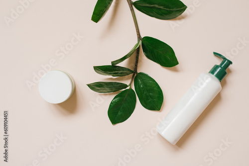 White cosmetic jar and a bottle of cream with a top view of the leaves of plants, a mock-up of the product design. Natural organic cosmetics