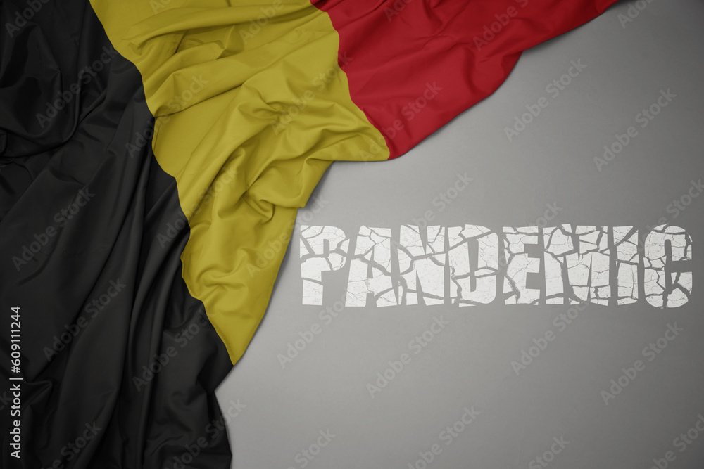 waving colorful national flag of belgium on a gray background with broken text pandemic. concept.