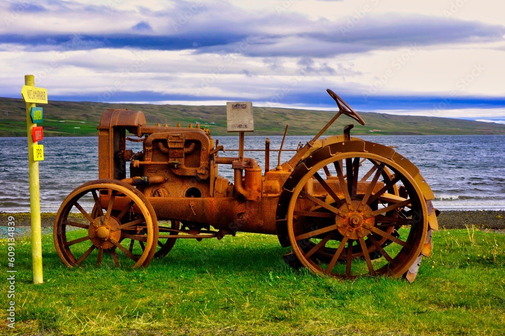 Alter rostiger Traktor auf einer grünen Wiese mit See im Hintergrund, auf Island 