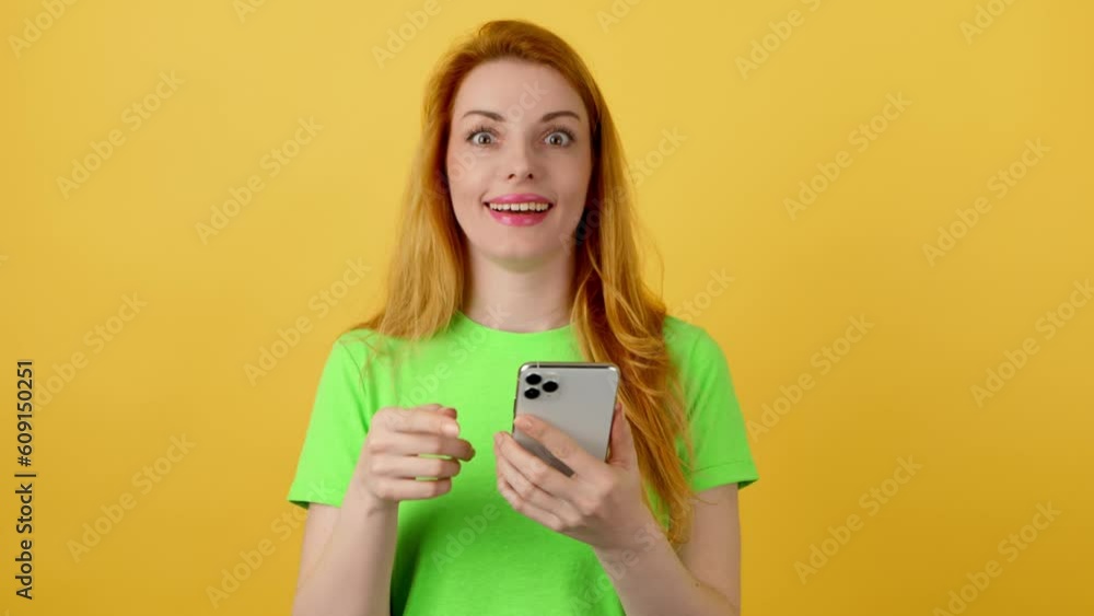 Surprised young woman pointing at mobile phone. Yes! Lady amazed excited with smartphone for social media, online streaming, news and internet, surprise face. Studio shot isolated on yellow background Surprised young woman pointing at mobile phone. Yes! Lady amazed excited with smartphone for social media, online streaming, news and internet, surprise face. Studio shot isolated on yellow background