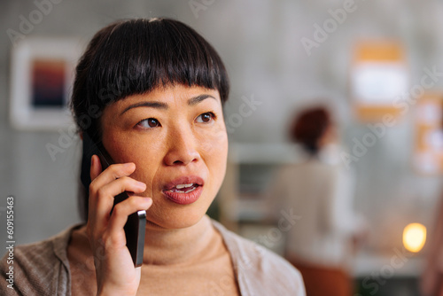 Close up portrait of Asian woman mildly shocked by news received over phone call.