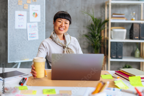 Young and happy Asian business woman joyfully using company computer while working in office.