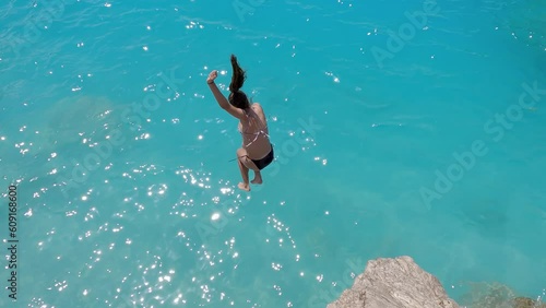 Young couple enjoy summer vacation jumping from high rock on Kathisma beach in Lefkada tuquoise water, slow motion photo