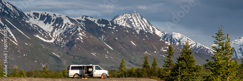 Epic camping area in Yukon Territory during summer time with magnificent snow capped mountains in background with van life, camper in foreground. 