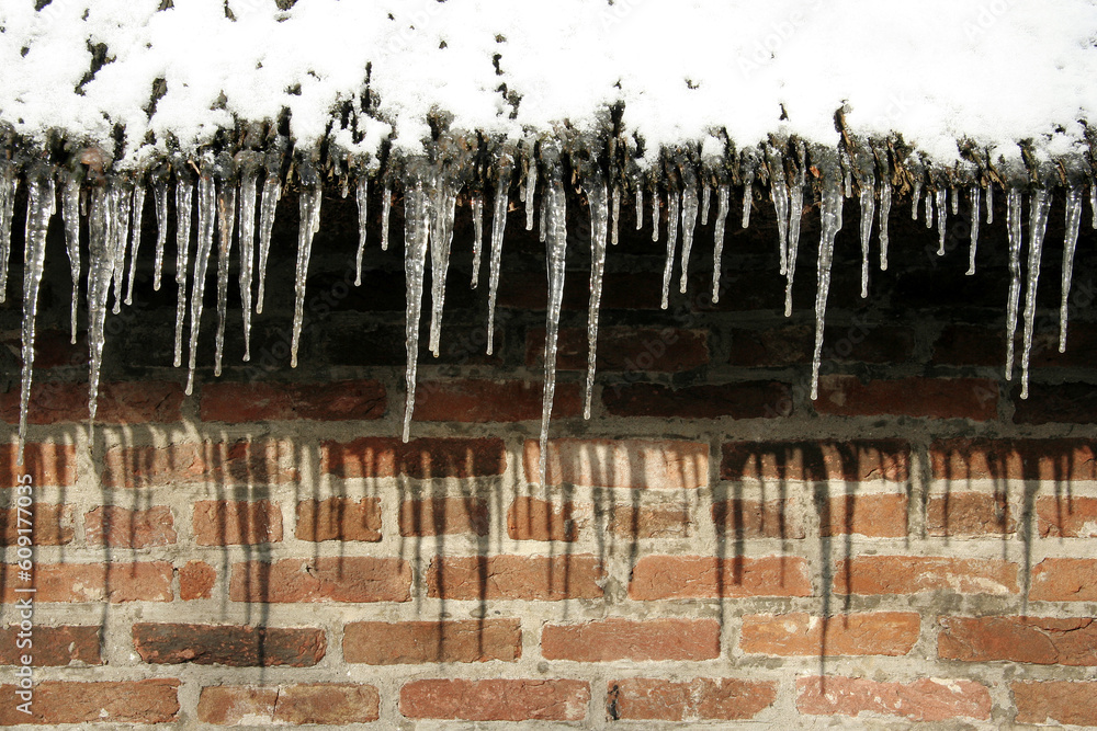 Icicles hanging on roofedge in front of brickwall Icicles hanging on roofedge in front of brickwall