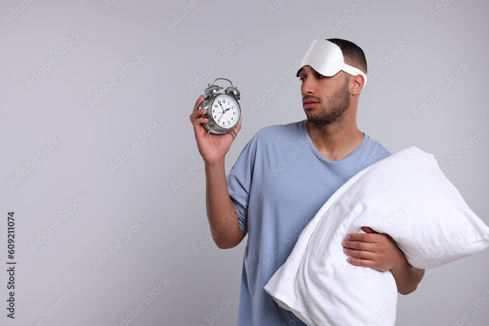 Tired man with pillow, sleep mask and alarm clock on light grey background, space for text. Insomnia problem Tired man with pillow, sleep mask and alarm clock on light grey background, space for text. Insomnia problem
