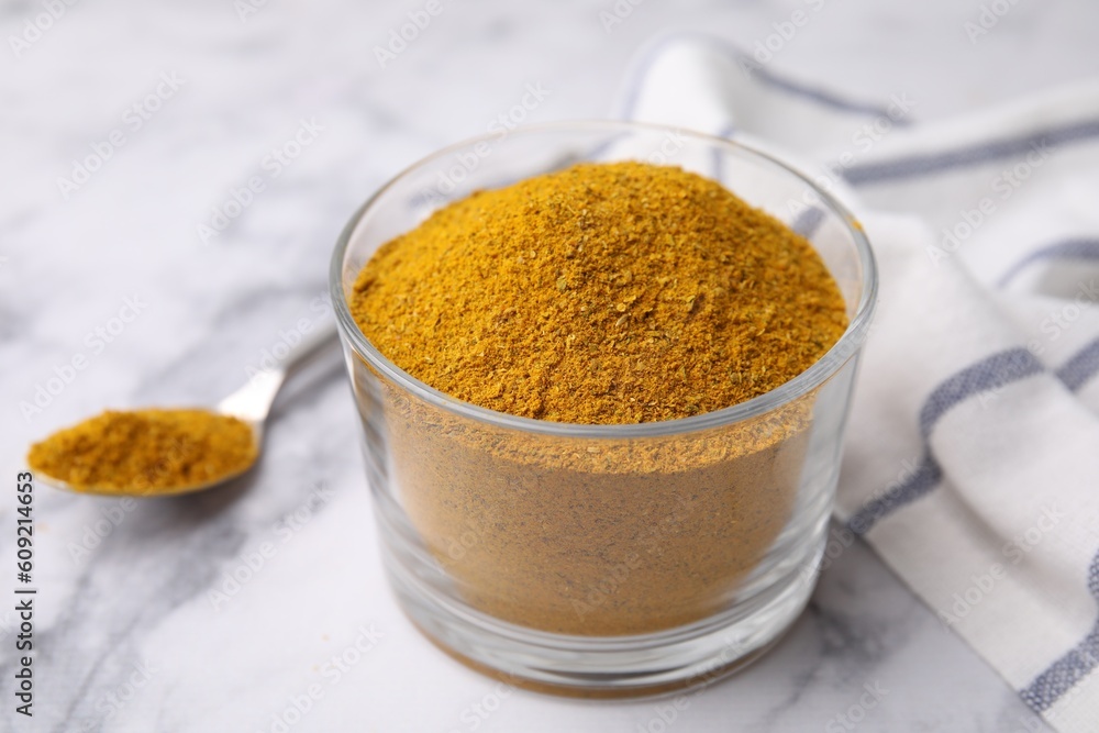 Glass with curry powder on white marble table, closeup
