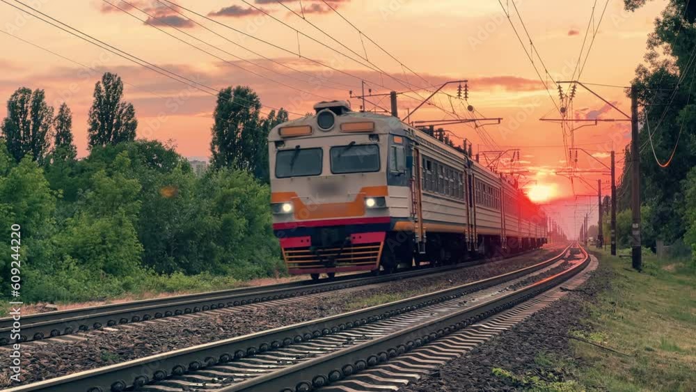 Suburban train travels through the countryside at a summer sunset. Front view. Long shot Suburban train travels through the countryside at a summer sunset. Front view. Long shot
