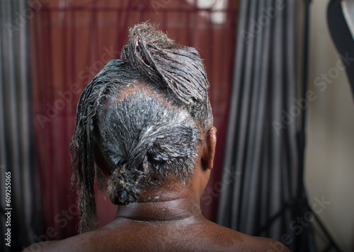 Hands of an African Nigerian stylist combing and applying relaxer cream to the  hair of a woman in saloon 