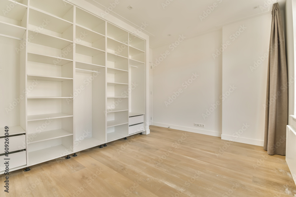 an empty room with white shelvings and wooden flooring in the middle part of the room, there is a large window an empty room with white shelvings and wooden flooring in the middle part of the room, there is a large window