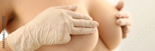 Woman with naked beautiful breasts closes nipples with gloved hands. Breast medical examination and mammologist concept photo