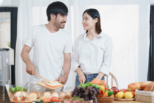 Smiling man hugging woman  two people standing and joyfully looking at each other. Young couple happily spending time in cozy modern kitchen at home.