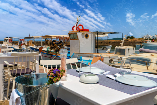 Fototapeta Naklejka Na Ścianę i Meble -  Tables and chairs of restaurant by waterfront with fishing boats in